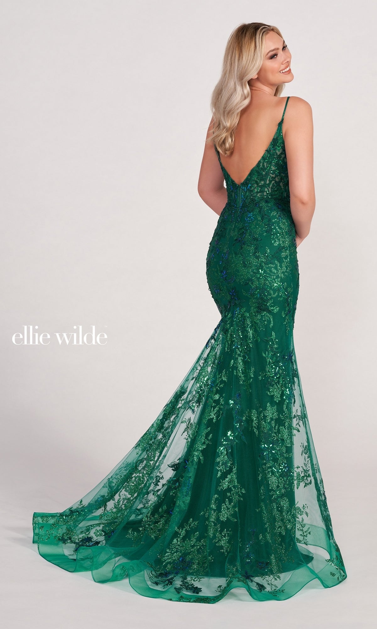 A woman models the Embroidered-Lace Ellie Wilde Prom Dress EW34061, a green floor-length mermaid gown with a low back and floral lace embroidery, against a simple light background.
